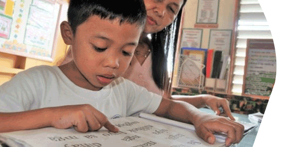 Teacher helping boy read in the Philippines