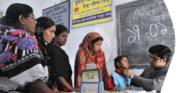 Health care worker checks child's throat at schools while mother and community looks on