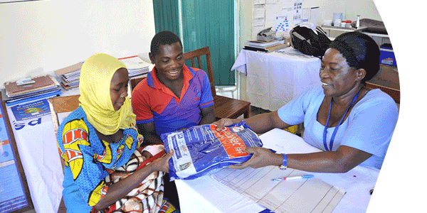 At the dispensary in Lwelu, Tanzania, Nurse Rehema Ngonyani distributes a mosquito net to clients Jaffar Ismaeli Liyoyo, 20, and his wife Fatuma Moussa Kanton, 19, with their one-week-old infant Noussofi.